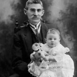 Portrait of a seated man holding a baby.  Family name Donohoo.