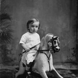 Studio portrait of a young child on a rocking horse.  Family name Powell.