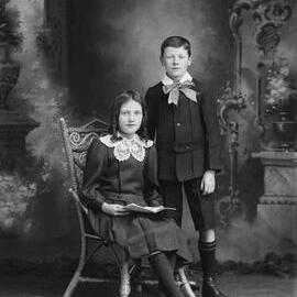 Studio portrait of a boy standing alongside seated girl.  Family name Kuhl.