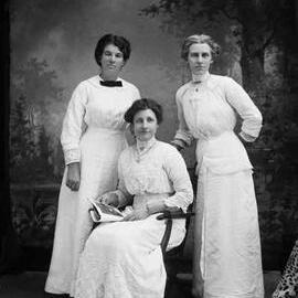 Studio portrait of three women wearing white dresses (one is possibly May Wilson).