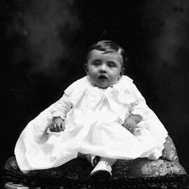 Studio portrait of a seated baby.  Family name ‘McCabe’.