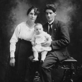 Studio portrait of a seated woman and man holding a baby.
