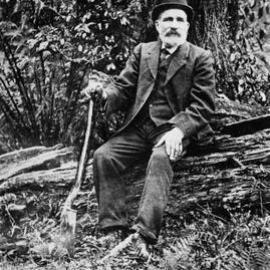 An unidentified man sitting on a log and holding a spade.