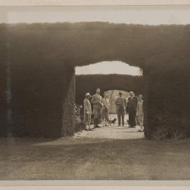 [Group of people and dogs posed next to hedge arch,] Ercildoune [Homestead]