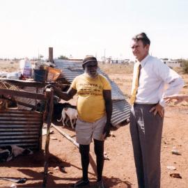 Malcolm Fraser and an Aboriginal Australian man standing alongside a dwelling in the Northern Territory.