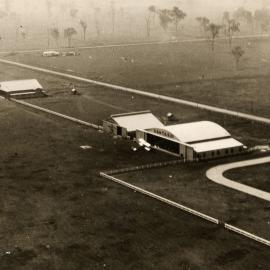 Aerial view of hangars and a biplane at an unknown location