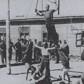 Unidentified prisoners of war camp: Practing gymnastics/circus skills watched on by crowd of men