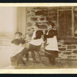 Three girls on rocking horse on verandah of house