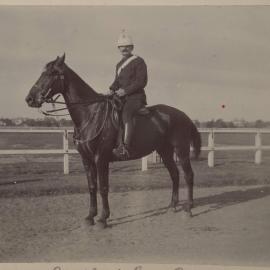 [Man wearing white helmet and tunic seated on horse]
