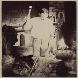 [Man creating horse shoe on anvil]