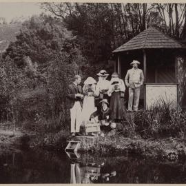 [Group of men and women posing beside lake]