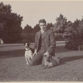 [Young man kneeling on grass with two dogs]