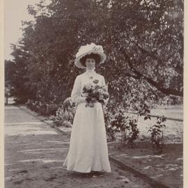[Woman wearing white dress in garden holding flowers]