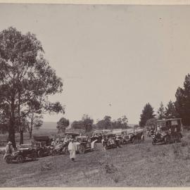 [Group of people standing near motor vehicles]