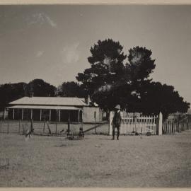 [Man standing at gates to homestead]