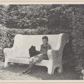 [Young boy and terrier dog posed on garden bench]