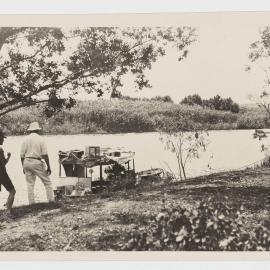 [Men observing boat from river bank]