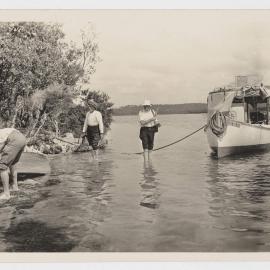 [Men wading in river near moored boat]